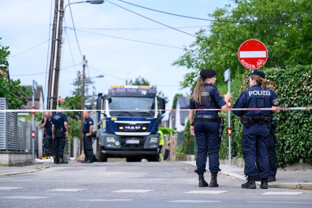 Polizisten sperren eine Straße ab, während ein Einsatzfahrzeug in einer Wohnstraße steht.