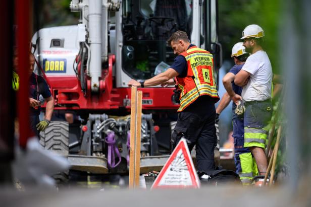 Feuerwehrleute und Bauarbeiter beraten sich vor einem Bagger an einer Einsatzstelle.
