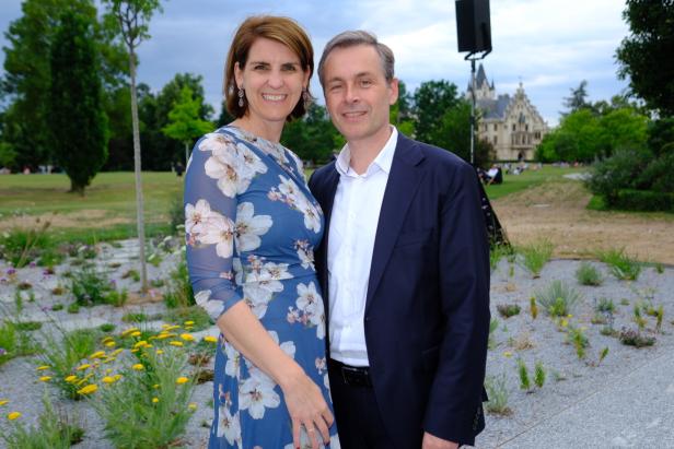 Ein lächelndes Paar steht im Park vor einem Schloss.
