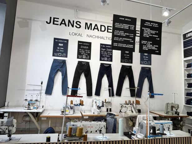 Schneiderwerkstatt für Jeans mit aufgehängten Hosen, mehreren Nähmaschinen und Preisschildern an der Wand.