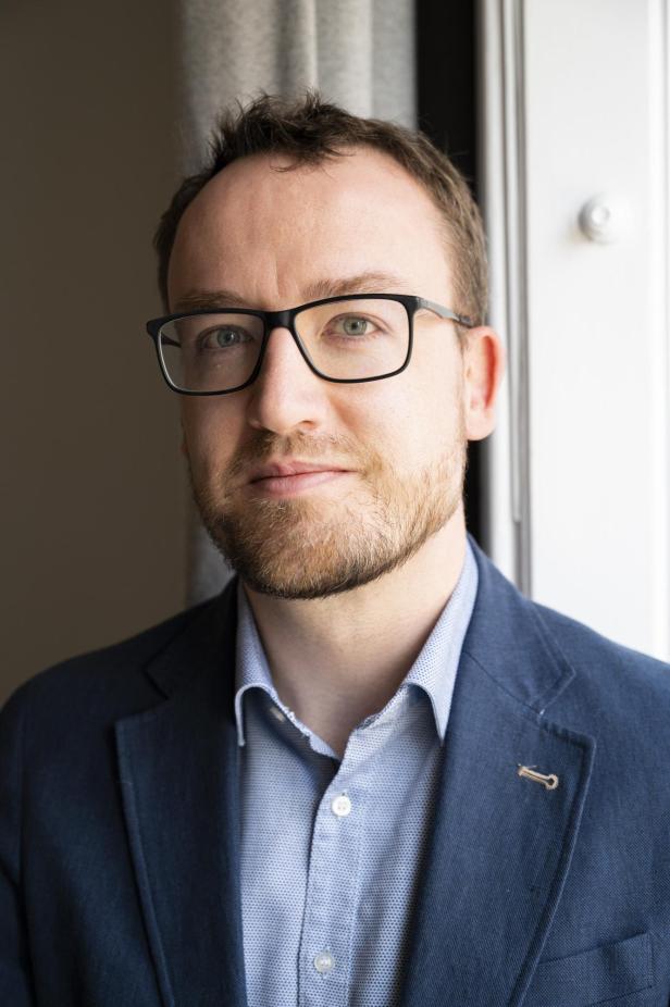 Porträt eines Mannes mit Brille im blauen Sakko am Fenster.