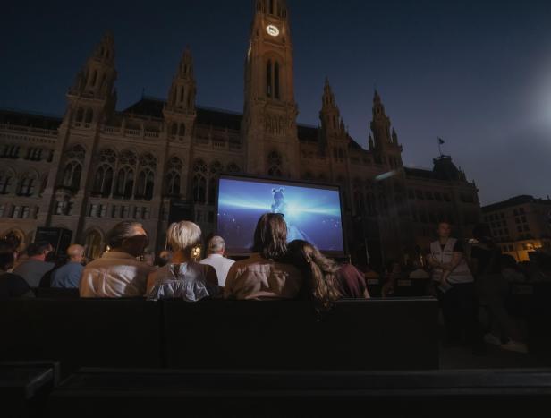 Publikum schaut abends vor dem Wiener Rathaus auf einer großen Leinwand einen Film.