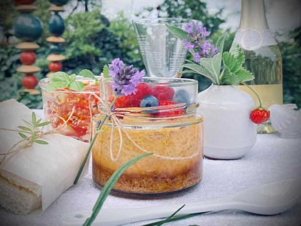 Im Glas servierter Cheesecake mit Beeren und eine Flasche Weißwein auf einer gedeckten Picknickdecke.