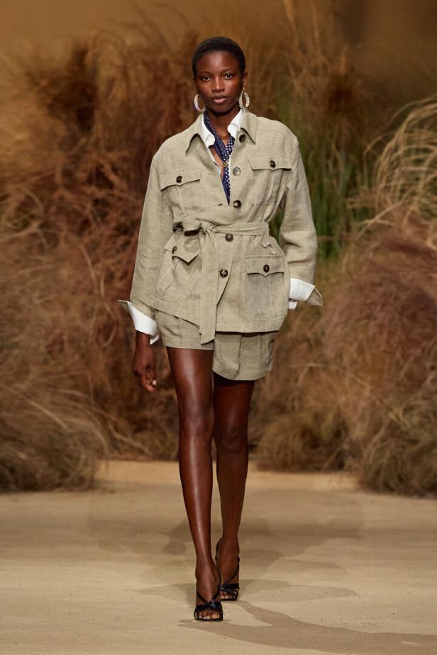 Model auf dem Laufsteg in beigem Safari-Outfit mit Gürtel und Shorts.