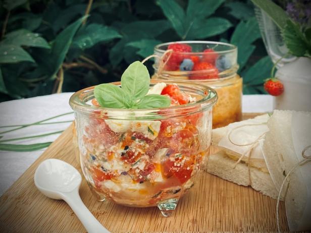 Tomaten-Feta-Salat mit Basilikum in Gläsern auf einem Holzbrett für ein Picknick.