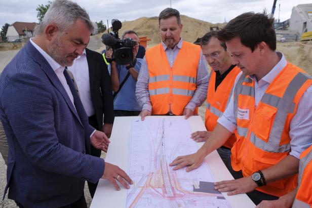 Mehrere Männer auf einer Baustelle besprechen einen Lageplan, während ein Kameramann filmt.
