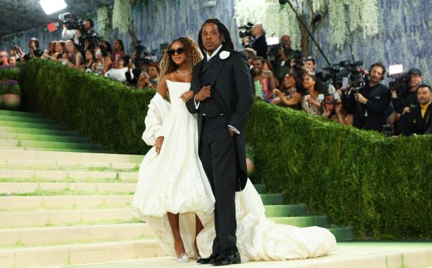 Beyoncé und Jay-Z posieren elegant in festlicher Kleidung auf einer Treppe vor einer Menschenmenge.