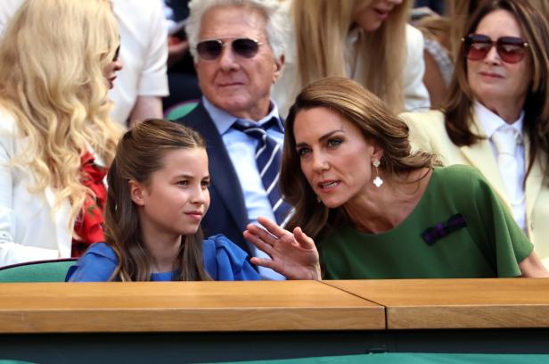Prinzessin Kate unterhält sich mit Prinzessin Charlotte auf der Tribüne von Wimbledon, während im Hintergrund Leute sitzen.