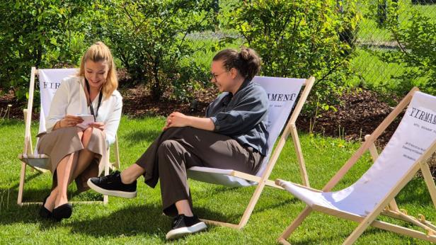 Zwei Frauen sitzen auf bedruckten Liegestühlen im Garten und unterhalten sich.