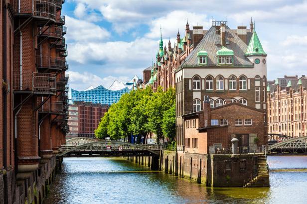 Historische Backsteinbauten an einem Kanal mit Brücken und grünen Türmen unter blauem Himmel.
