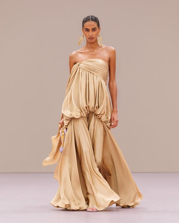 Eine Frau am Laufsteg mit aufgebauschtem goldenen Kleid