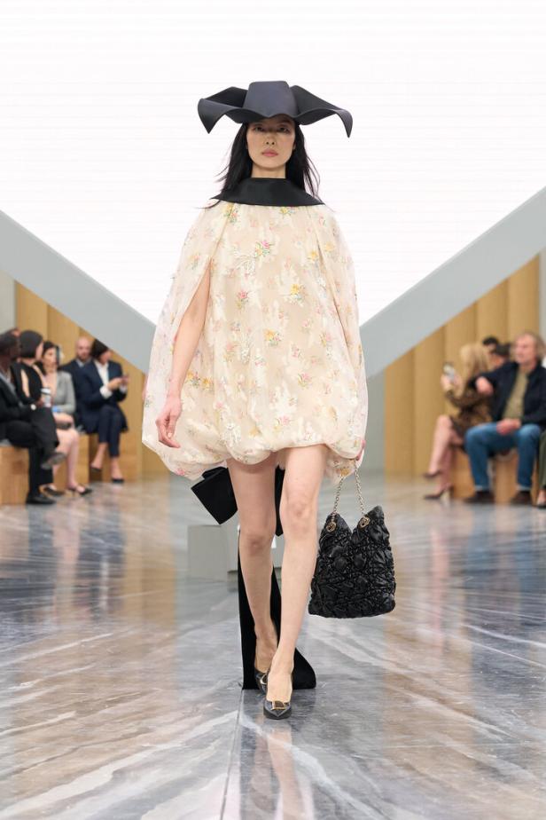 Ein Model am Laufsteg mit aufgebauschtem Kleid und einem schwarzen Hut auf dem Kopf