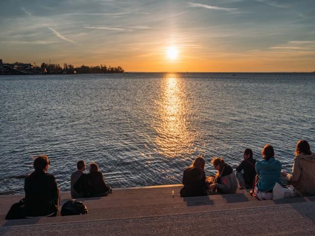 Menschen sitzen an Uferstufen und schauen dem Sonnenuntergang über dem Wasser zu.