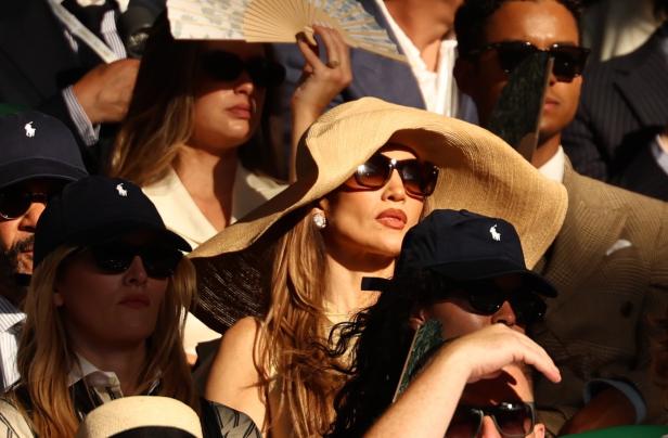 Jennifer Lopez trägt einen großen Strohhut und eine Sonnenbrille inmitten von Zuschauern auf der Tribüne.