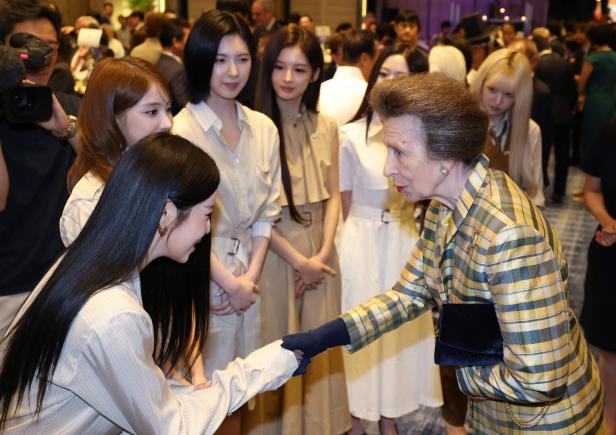 Prinzessin Anne in der britischen Botschaft in Seoul, Südkorea Prinzessin Anne schüttelt einer jungen Frau die Hand, während Mitglieder der K-Pop-Gruppe NMIXX in hellen Outfits danebenstehen.