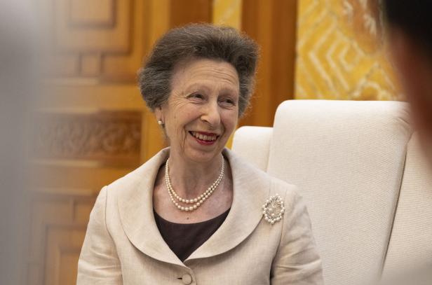 Prinzessin Anne Prinzessin Anne lächelt freundlich in einem beigen Blazer mit Perlenkette und einer blattförmigen Brosche vor einem hellen Hintergrund.