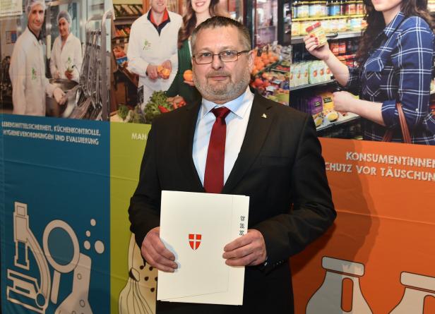 Andreas Kutheil hält Unterlagen vor einem farbigen Lebensmittel- und Verbraucherschutz-Hintergrund.