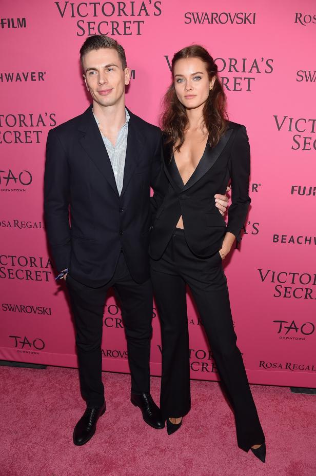 Ein Mann und eine Frau posieren auf einem roten Teppich vor einer Victoria's Secret Werbewand.