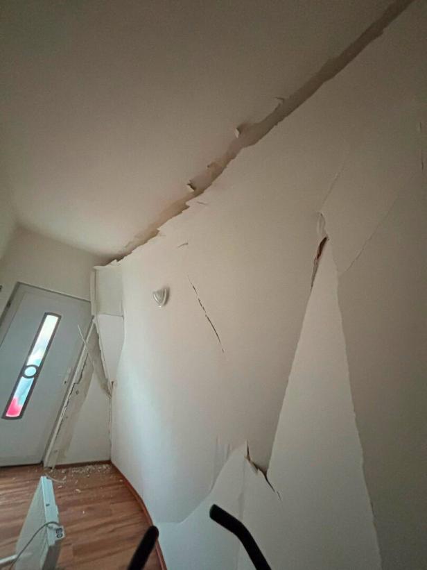 Stark beschädigte Wand mit großen Rissen und abblätterndem Putz im Flur.