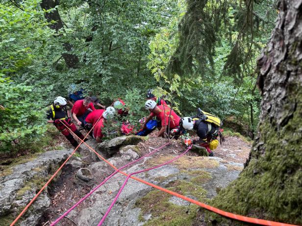 Bergretter sichern verletzte Wanderin an steilem Waldhang.