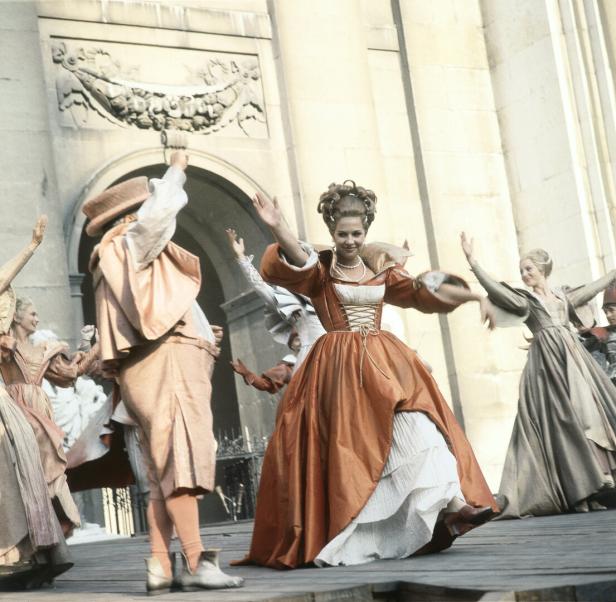 Salzburger Festspiele Schauspieler in historischen Kostümen tanzen vor einem steinernen Torbogen.