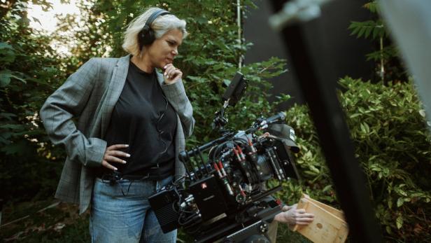 Olivia Retzer mit Kopfhörern beobachtet draußen ein Filmset mit Kamera.