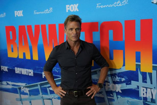 David Charvet steht vor einer blauen Wand mit dem Baywatch-Logo und Fox-Schriftzügen.