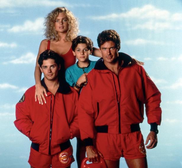 David Hasselhoff und weitere Rettungsschwimmer der Serie Baywatch posieren vor einem hellblauen Himmel. Bild aus den Neunzigern mit Eddie, Shauni und seinem Sohn Hobie