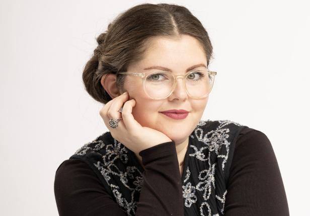 Eine Frau mit Brille vor einem weißen Hintergrund.