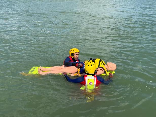 Samariterbund, Wasserrettung, Ertrunkene Zwei Rettungsschwimmer in Schutzkleidung bergen eine Übungspuppe auf einem Rettungsbrett aus dem Wasser.
