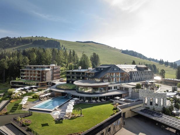 Wellnesshotel mit Pool vor grüner Almkulisse.
