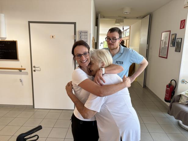 Zwei Frauen und ein Mann umarmen sich herzlich in einem hellen Flur.