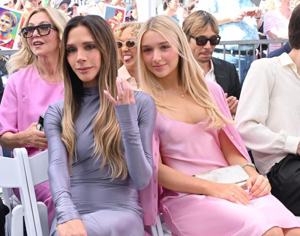 Victoria Beckham sitzt neben einer jungen blonden Frau in einem rosa Kleid bei einer öffentlichen Veranstaltung.