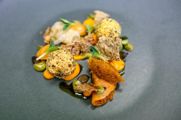 Fein angerichtetes Gourmetgericht mit würzigen Kugeln, Saucenpunkten und Kräutern auf dunklem Teller.