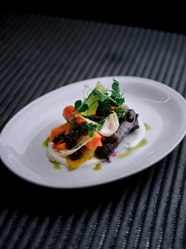 Fein angerichtetes Gourmetgericht mit Gemüse, Saucen und Kräutern auf weißem Teller.