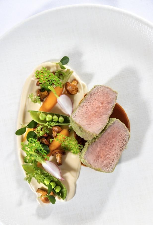 Zwei rosarote Fleischscheiben mit Gemüse, Erbsen, Pilzen und Kräutern auf heller Sauce angerichtet.
