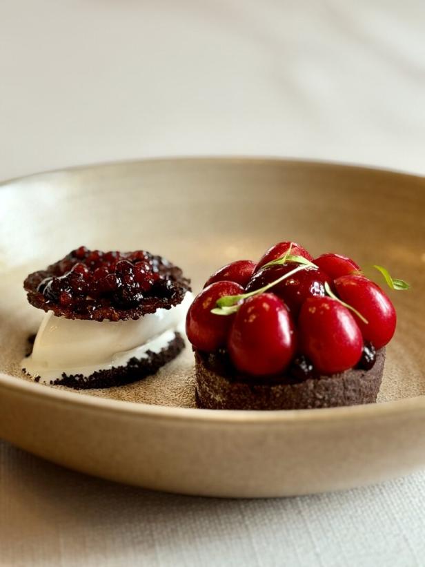 Zwei kunstvoll angerichtete Desserts mit glänzenden roten Früchten in einer goldenen Schale.