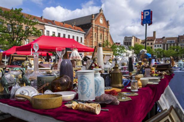 Flohmarkt mit vielen Antiquitäten auf einem roten Tisch vor historischen Häusern und einer Kirche.