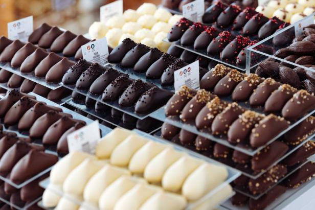 Mehrere Etagen mit kunstvoll dekorierten Schokoladenpralinen in verschiedenen Sorten und Farben auf Glasplatten.
