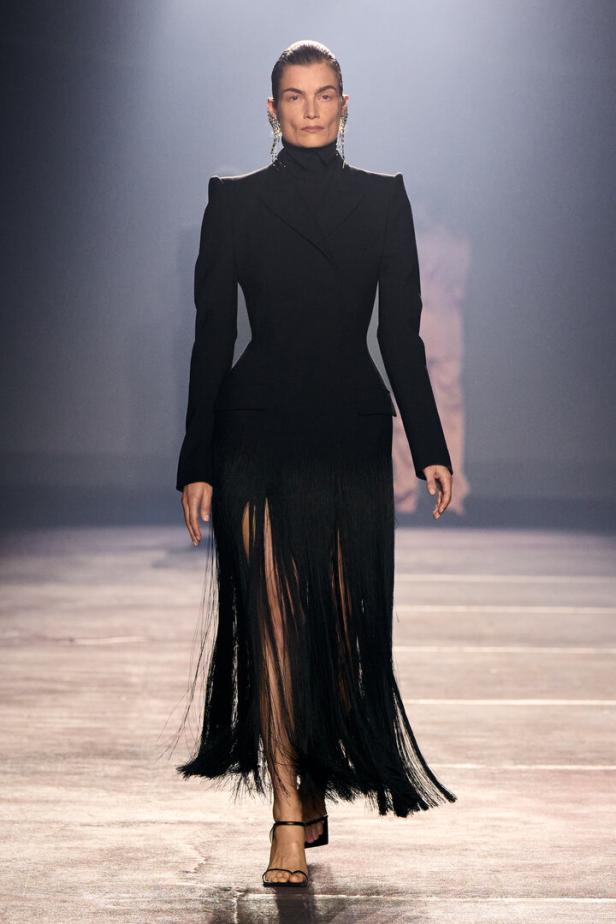 Modell in schwarzem, hochgeschlossenem Couture-Kleid mit Fransenrock auf dem Laufsteg.