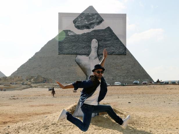 Mann springt vor der Cheops-Pyramide, hinter ihm eine optische Täuschung mit riesiger Hand und schwebendem Stein.