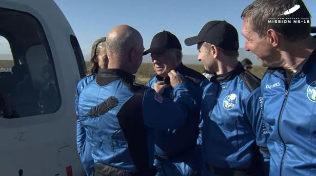 Jeff Bezos gratuliert William Shatner nach der New Shepard Mission NS-18, während beide blaue Fluganzüge tragen.