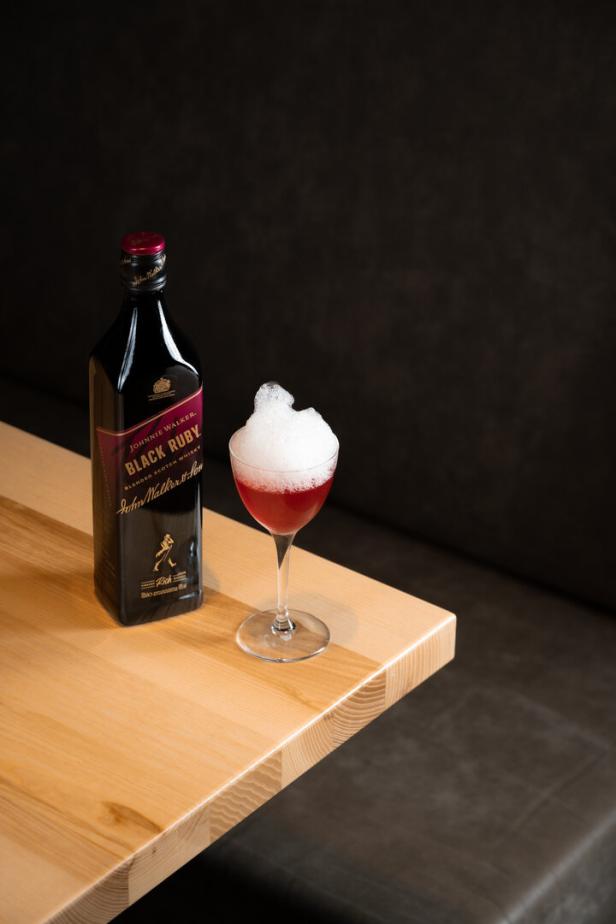 Cocktail Vanilla Sky steht neben einer Flasche Black Ruby von Johnny Walker auf einem Tisch