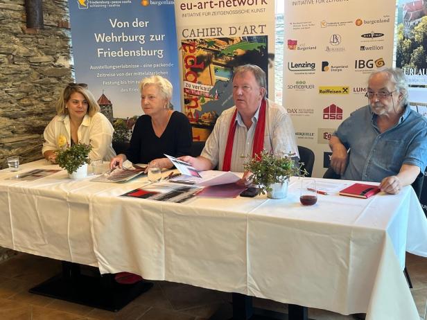 Vier Personen sitzen an einem Tisch bei einer Pressekonferenz vor Werbebannern.