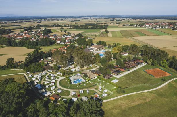 Luftaufnahme eines Campingplatzes mit Wohnwagen, Pool und Tennisplatz inmitten von Feldern und Dörfern.