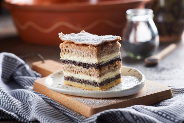 Mehrschichtiger Kuchen mit Puderzucker auf einem Teller, auf Holzbrett vor rustikalem Hintergrund.