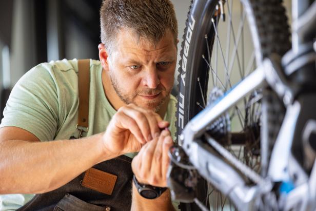 Ein konzentrierter Mechaniker in einer Werkstattschürze repariert die Schaltung eines Mountainbikes.