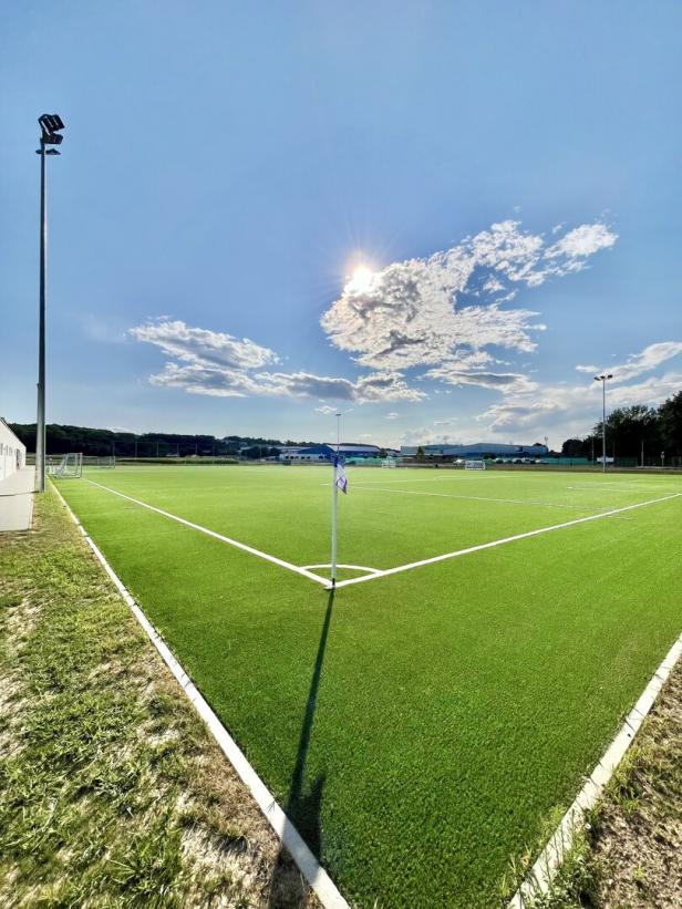 Leerer Kunstrasen-Fußballplatz bei Sonnenschein mit Eckfahne und blauem Himmel.