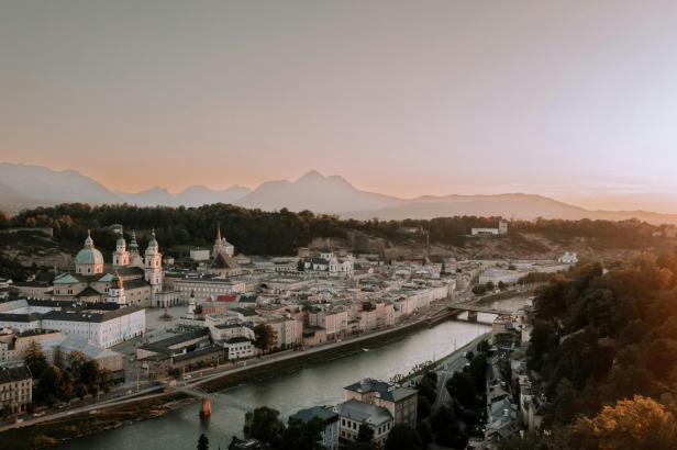 Blick über Salzburg mit Fluss, Altstadt und Bergen im Abendlicht.