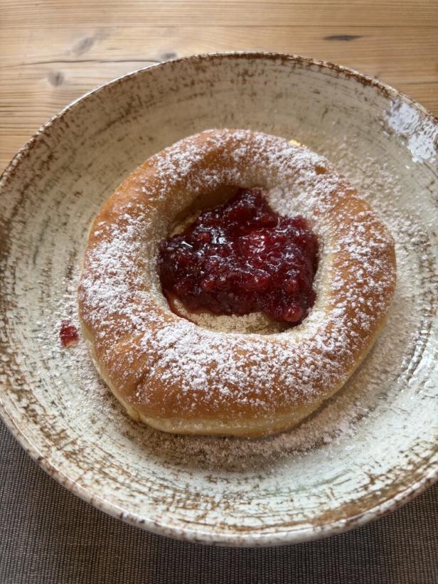 Gefüllter, mit Puderzucker bestäubter Hefekrapfen mit roter Marmelade in einer Schale.